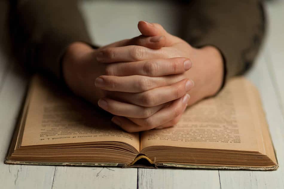 Open Bible with hands in prayer, illustrating a moment of contemplation and connection to faith. Open Bible with hands in prayer, illustrating a moment of contemplation and connection to faith.