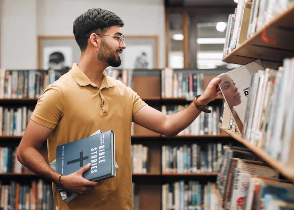 man with dark hair and a yellow shirt pulls books off a library shelf man with dark hair and a yellow shirt pulls books off a library shelf
