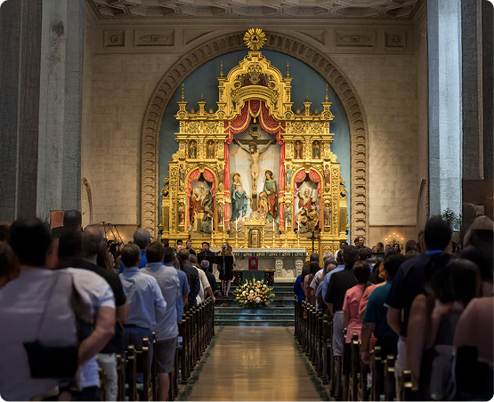 Congregation seated in pews facing an ornate golden Orthodox iconostasis in a church interior.