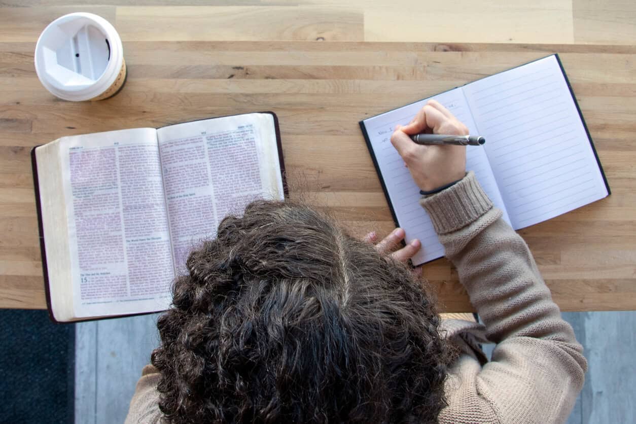 Person studying with an open book and notebook on a wooden desk.