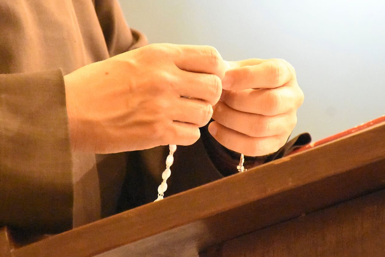 Hands holding a rosary with beads draped between the fingers.