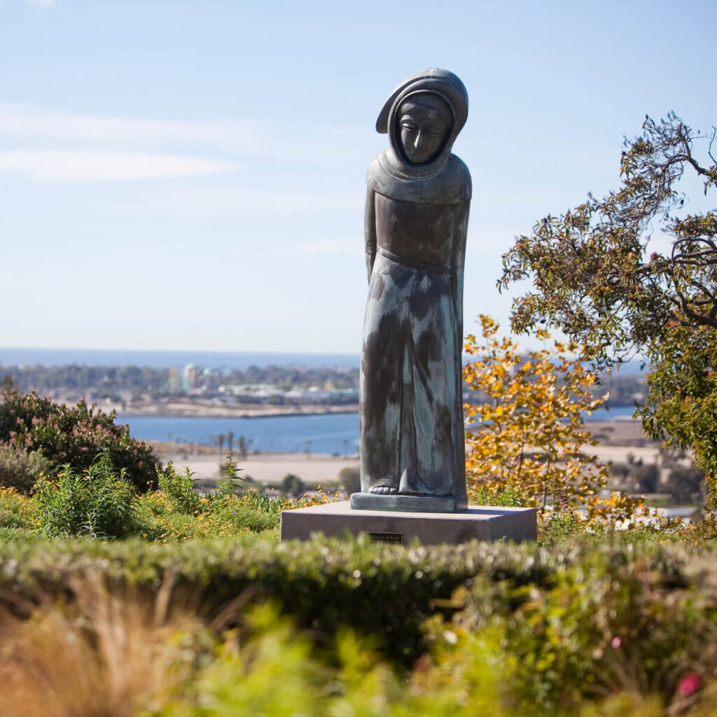 a statue of st.francis sits in a green park overlooking a body of water