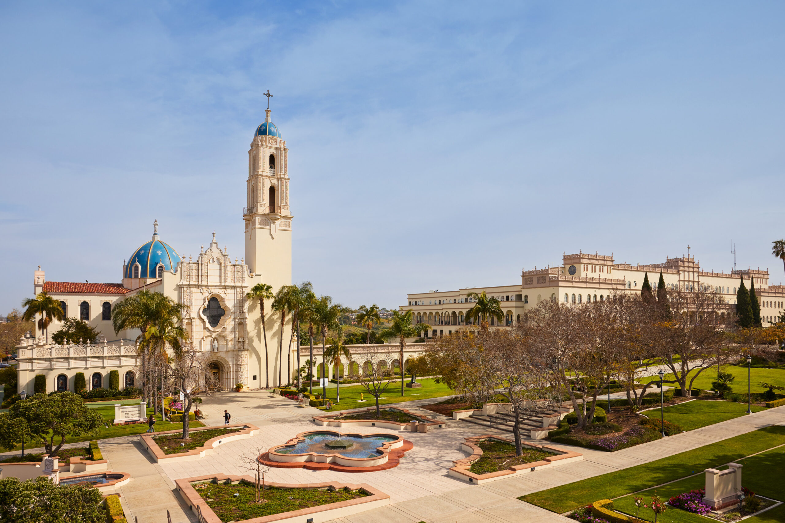 A Spanish colonial-style cathedral with a tall bell tower and blue dome overlooks a manicured plaza.