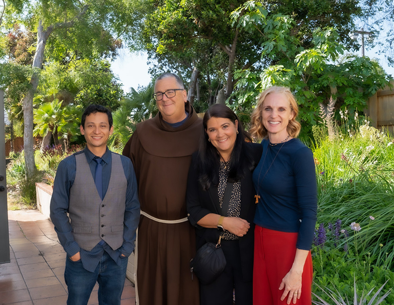 Four people stand together on a tree-lined path outdoors.