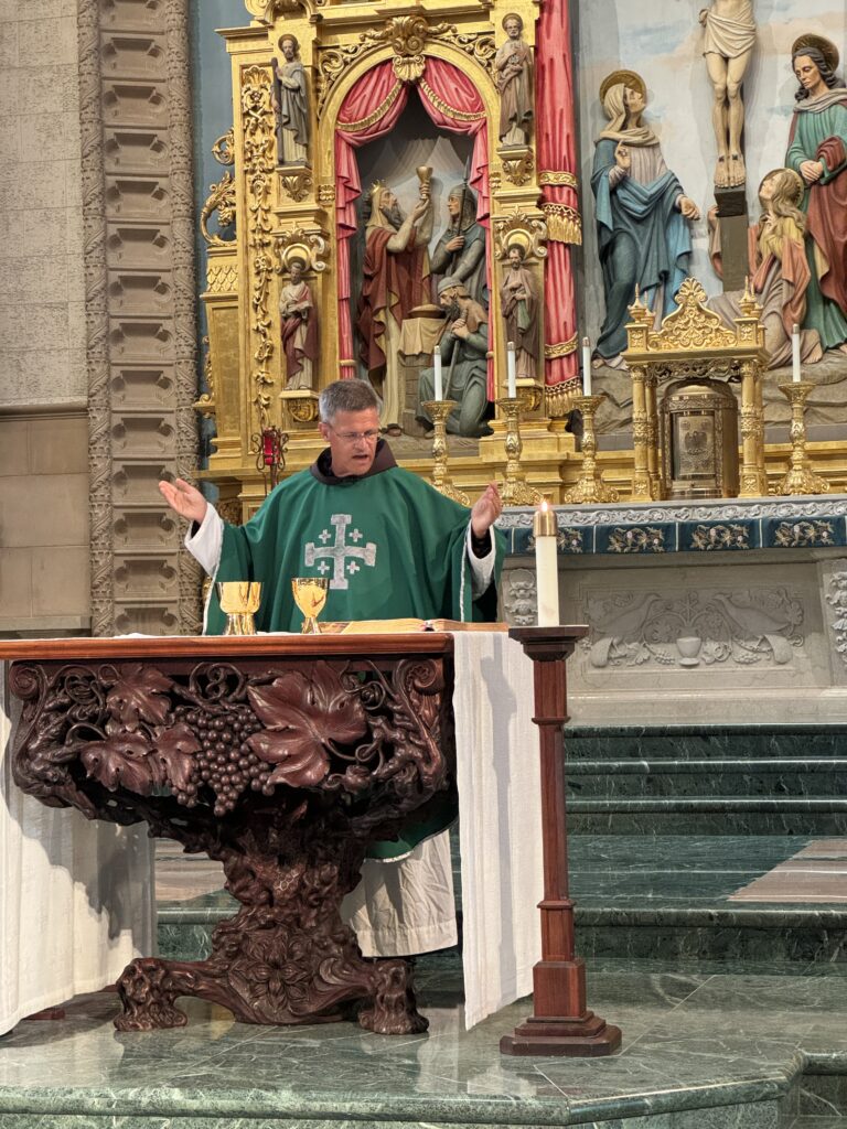 Priest in green vestments celebrates Mass at an ornate altar in a Catholic church.