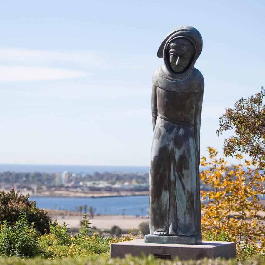 a statue of st.francis sits in a green park overlooking a body of water
