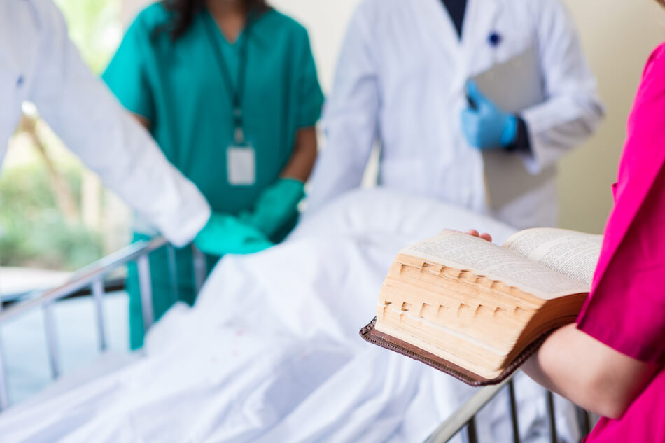 hospital champlain reading from a bible to a patient at the hospital surrounded by doctors